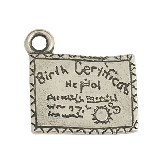 Close-up of a small silver-tone rectangular charm engraved with 'Birth Certificate' and a decorative border.