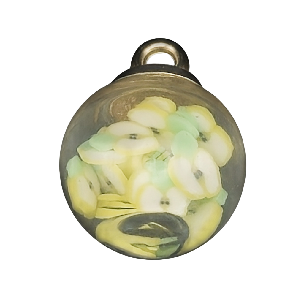 Close-up of a small glass globe charm filled with tiny yellow and green fruit slices.