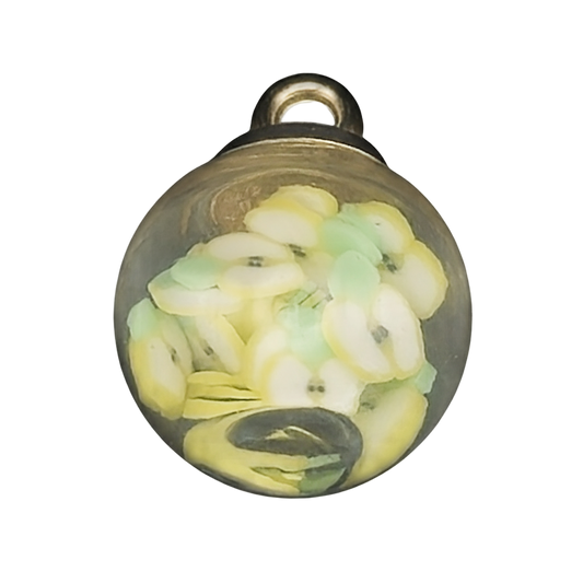 Close-up of a small glass globe charm filled with tiny yellow and green fruit slices.