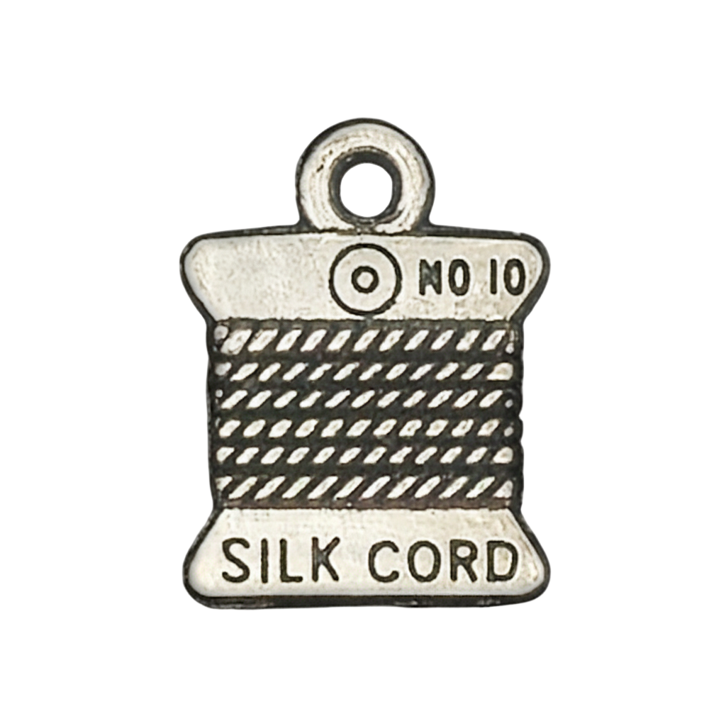 Close-up of a silver-tone charm shaped like a silk cord spool with 'SILK CORD' and 'No 10' text.