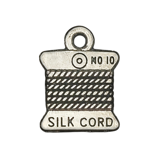 Close-up of a silver-tone charm shaped like a silk cord spool with 'SILK CORD' and 'No 10' text.