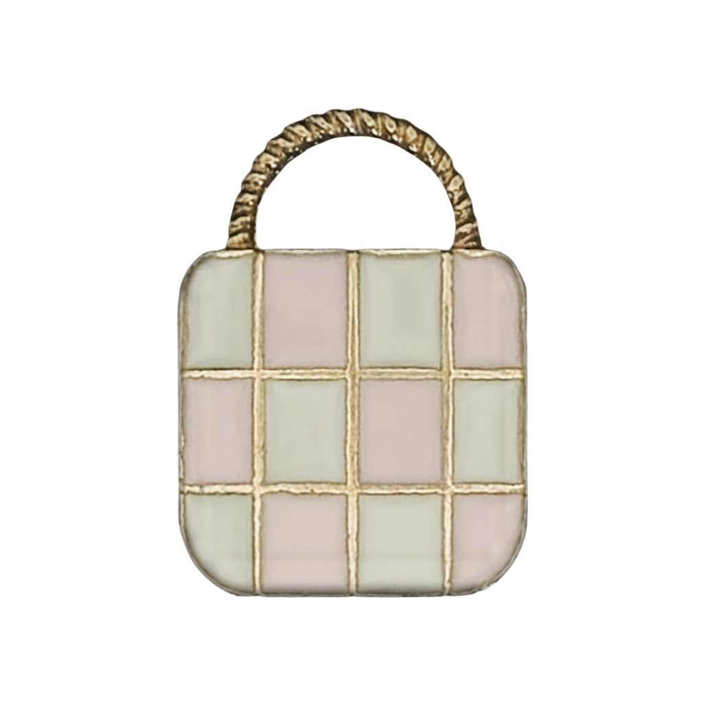 close-up of enamel handbag charm with pink and cream checkered front and black handle on black background