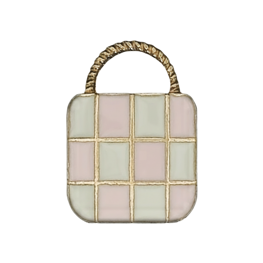 close-up of enamel handbag charm with pink and cream checkered front and black handle on black background