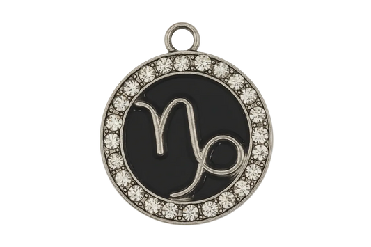 Close-up of a round black charm with a silver Capricorn symbol and clear rhinestone border on a black background.