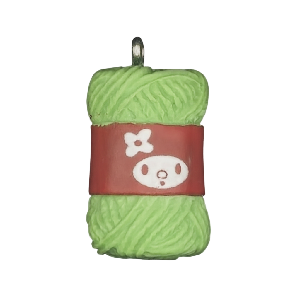 close-up of green yarn skein charm with red label and white face icon on black background