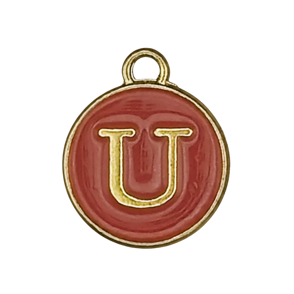 Close-up of a round red enamel charm with a gold letter U on a black background.