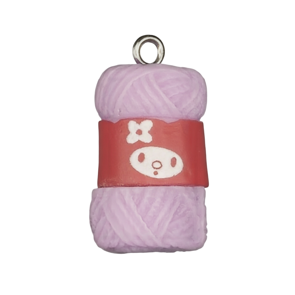 Close-up of a lavender yarn skein charm with a red label showing a simple white face graphic on a black background.