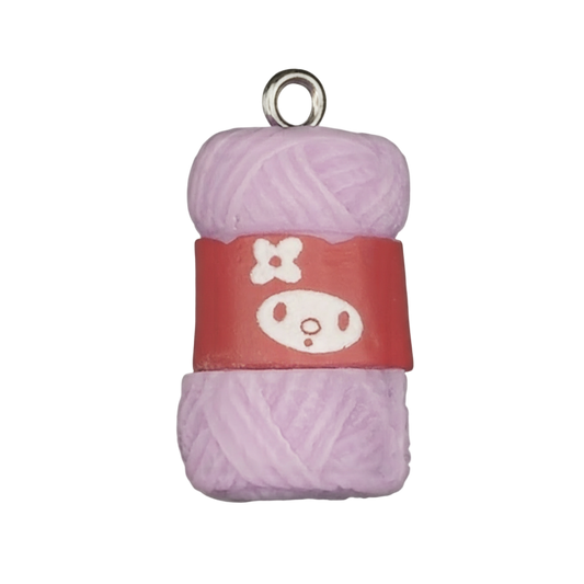 Close-up of a lavender yarn skein charm with a red label showing a simple white face graphic on a black background.