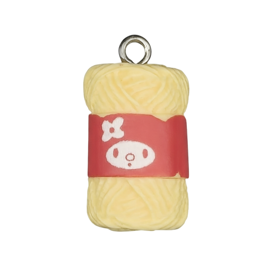 close-up of yellow yarn skein charm with red label on black background