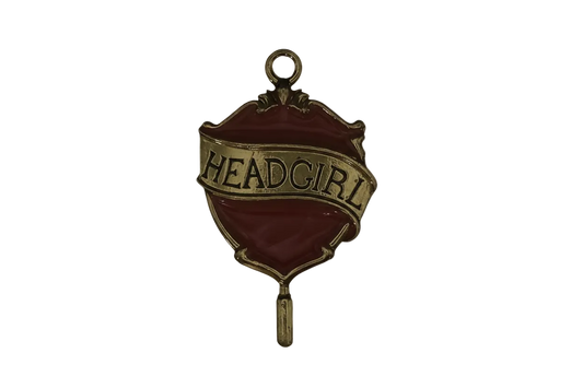 close-up of red and gold 'HEAD GIRL' badge charm on black background