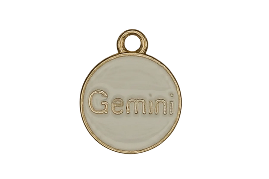 close-up of round cream enamel charm with gold 'Gemini' text