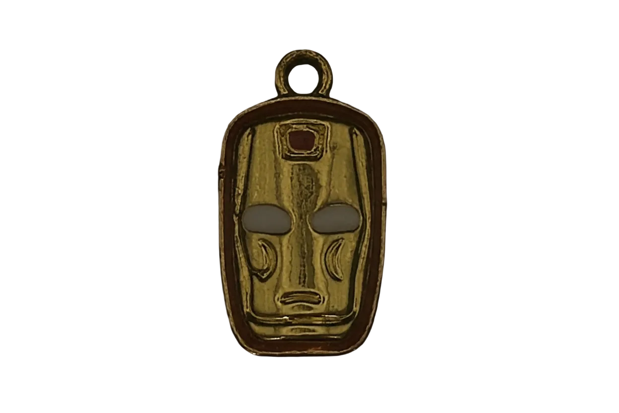Close-up gold-tone mask face charm with a small red detail on a black background.