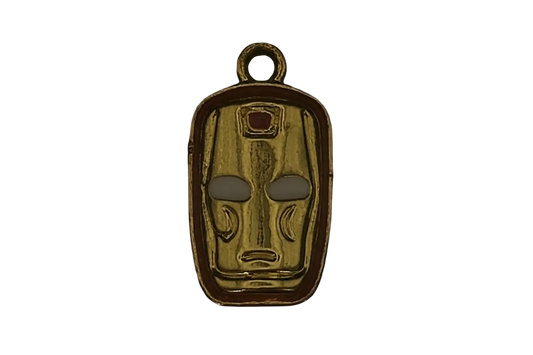 Close-up gold-tone mask face charm with a small red detail on a black background.