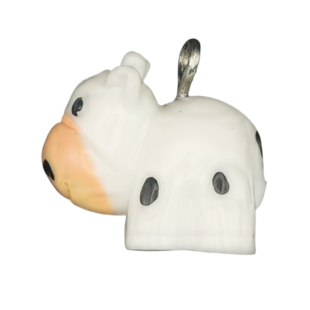 close-up of a small white cow-shaped charm with black spots and an orange muzzle