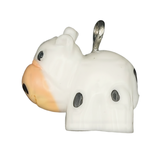 close-up of a small white cow-shaped charm with black spots and an orange muzzle