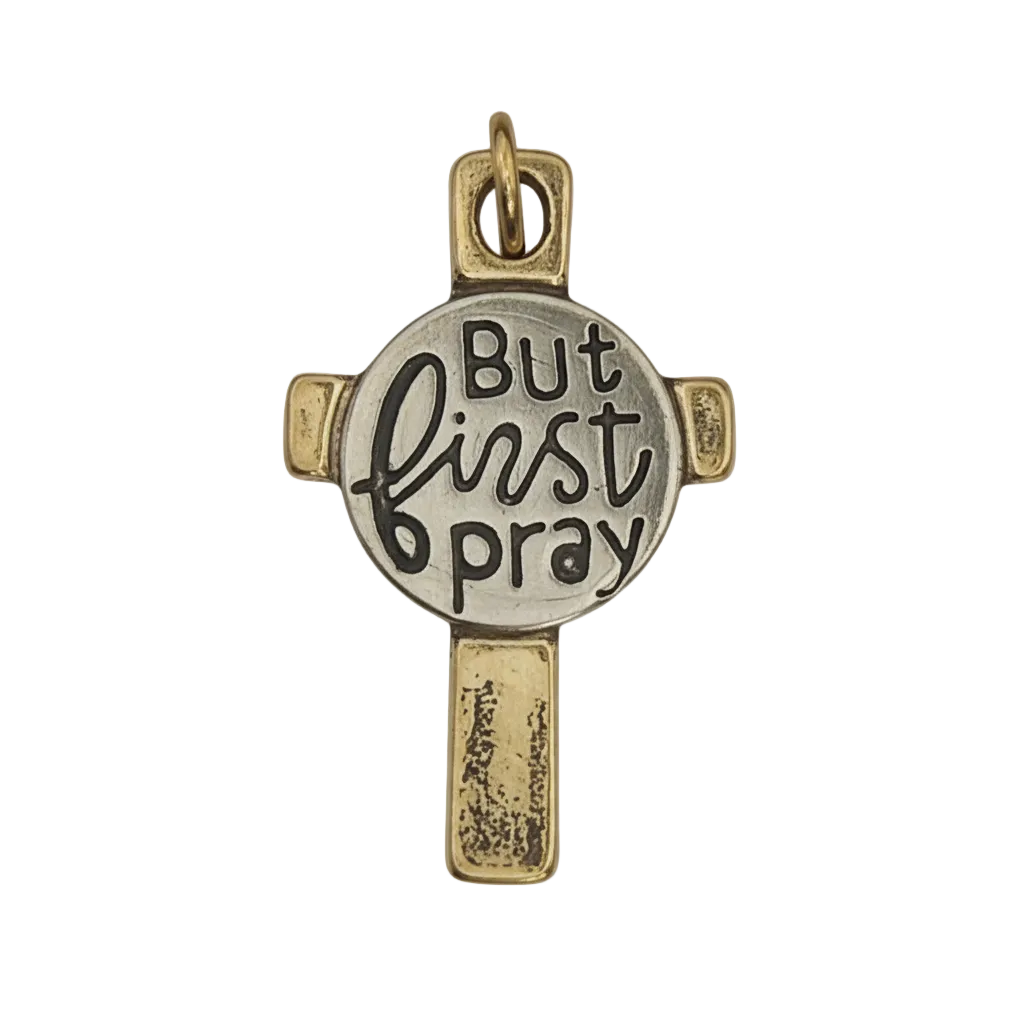 close-up of two-tone cross charm with 'But first pray' text on round center