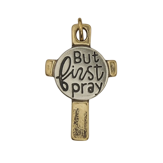 close-up of two-tone cross charm with 'But first pray' text on round center
